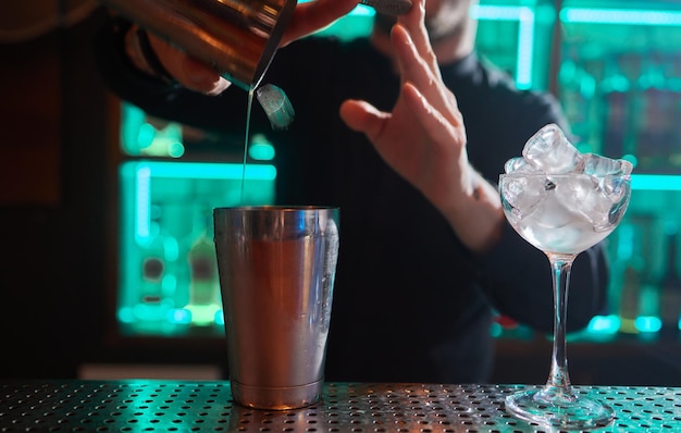 Barman w koszuli i fartuchu robi napój alkoholowy z lodem w kieliszku koktajlowym