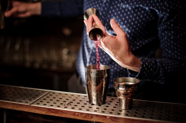 Barman wlewa do shakera porcję różowego napoju alkoholowego