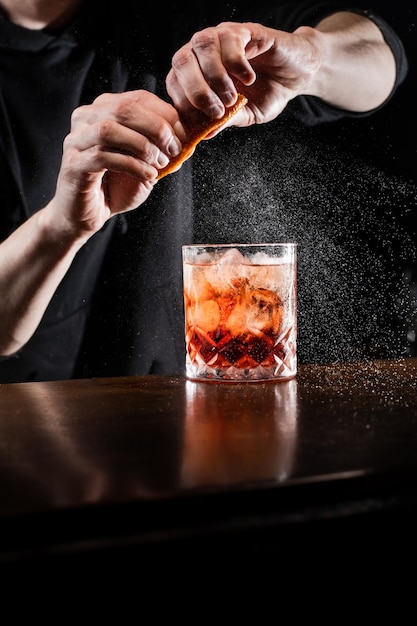 Barman wyciska skórkę pomarańczową i skrapia sokiem Negroni w szklance Barman przygotowuje klasyczny koktajl Negroni w barze