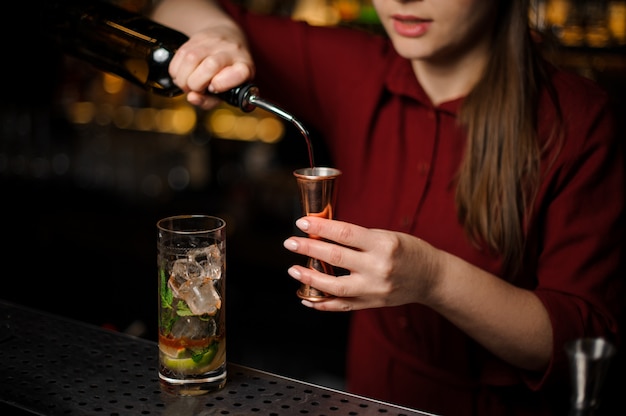 Barmanka przygotowuje mojito, dodając ciemny rum i używając wyposażenia baru