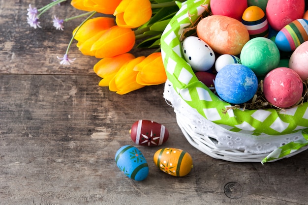 Barwioni Easter jajka w koszu i kwiatach na drewnianej powierzchni
