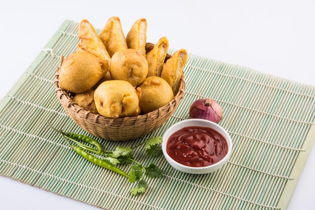 Batata vada lub aalu bonda i pakode chleb serwowane w koszyku trzciny z keczupem, cebulą i kolendrą na białym tle. Indyjskie przekąski