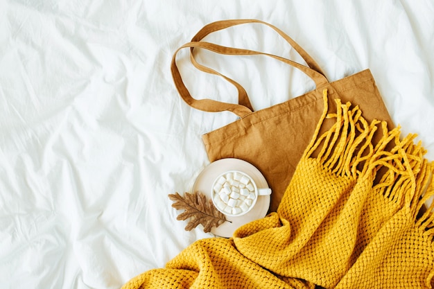Bawełniana eko torba z filiżanką kawy i żółtym dzianinowym szalikiem na łóżko. Koncepcja jesień.
