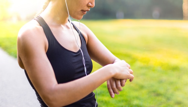 Bawi się azjatykciej kobiety słucha muzyka z hełmofonami podczas gdy patrzejący zegarek outdoors