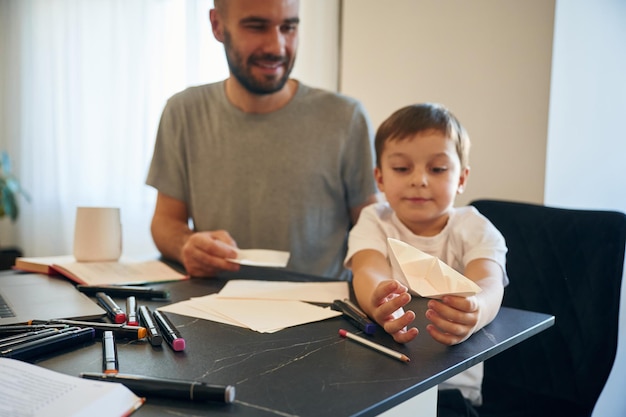 Zdjęcie bawiąc się łodzią origami ojciec i syn są w domu przy stole
