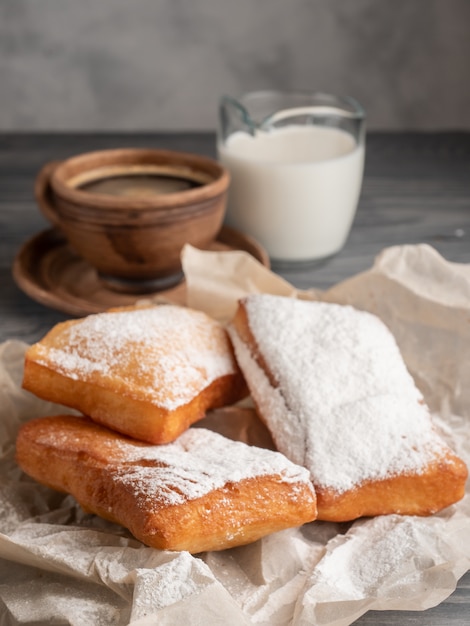 Beignet posypane cukrem pudrem na drewnianym stole z kawą i mlekiem.