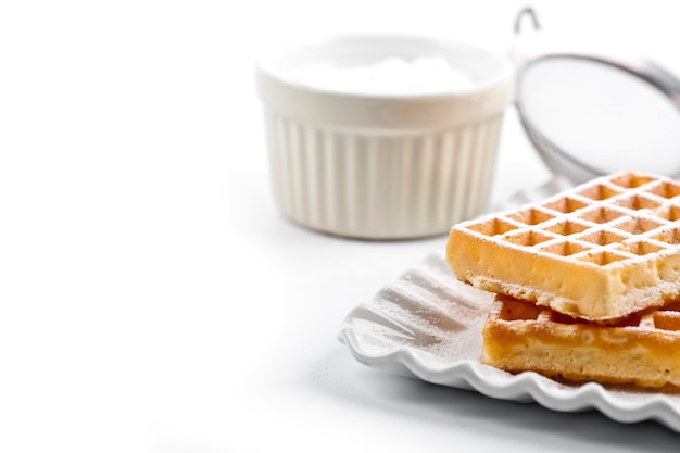 Zdjęcie belgia waffers z cukrem w proszku na ceramicznym talerzu i sitko na białym stole.