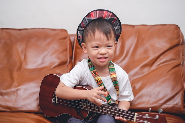 Berbeć Chłopiec Dziecko Jest Ubranym Kapeluszowego Chwyt & Bawić Się Hawajską Gitarę Lub Ukulele W żywym Pokoju