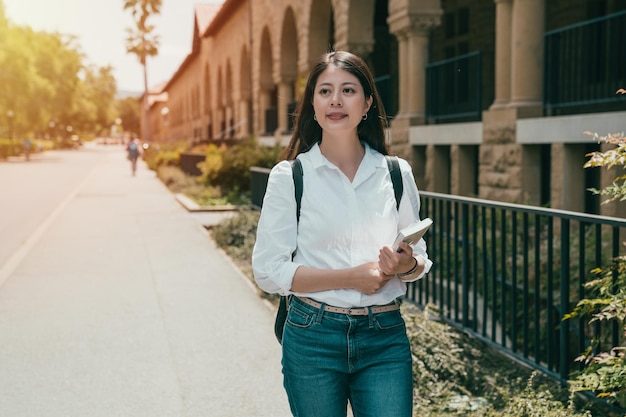 beutiaul studentka zagraniczna trzymająca swoją książkę i kierująca się do klasy przedmiotu.