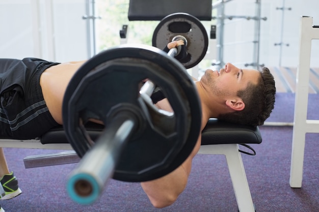 Bez koszuli bodybuilder podnosi ciężkiego barbell ciężaru lying on the beach na ławce