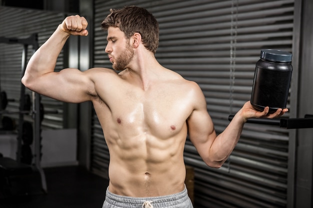 Bez koszuli mężczyzna pokazuje bicepsy i trzyma puszkę przy crossfit gym