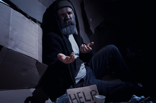 Bezdomny brodaty mężczyzna siedzi na pudłach na ulicy i prosi o pomoc. Potrzebna osoba bezdomna prosi o pieniądze na wyżywienie i nocleg.