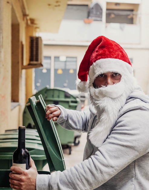 Bezdomny Mikołaj pije wino i grzebie w koszach na śmieci.