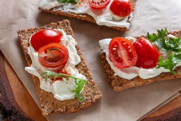 Bezglutenowe organiczne krakersy pomidorowe z pastą bez laktozy i świeżymi pomidorami na tle płytek ceramicznych.