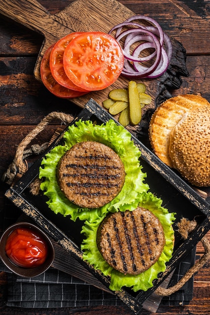 Zdjęcie bezmięsne burgery na bazie roślin z wegetariańskimi bezmięsnymi pieczonymi kotletami kotletami z pomidorami i cebulą w drewnianej tacy do serwowania drewniane tło widok z góry