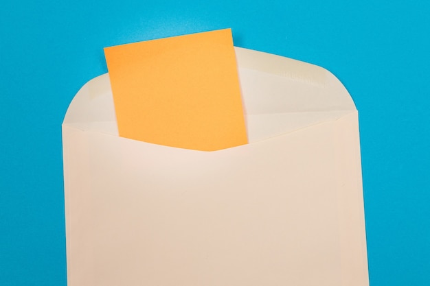 Beżowa koperta z pustym pomarańczowym arkuszem papieru w środku