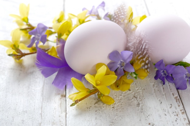 Beżowe jajko z piórami przepiórczymi, żółte i liliowe kwiaty na drewnianym, odrapanym szyku