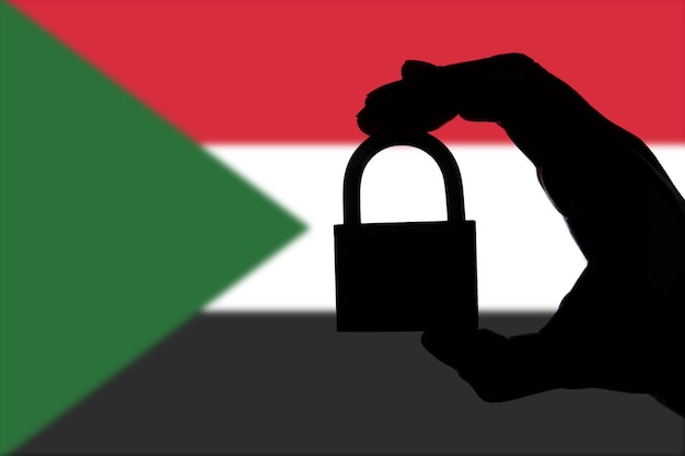 Bezpieczeństwo Sudanu Sylwetka ręki trzymającej kłódkę nad flagą narodową
