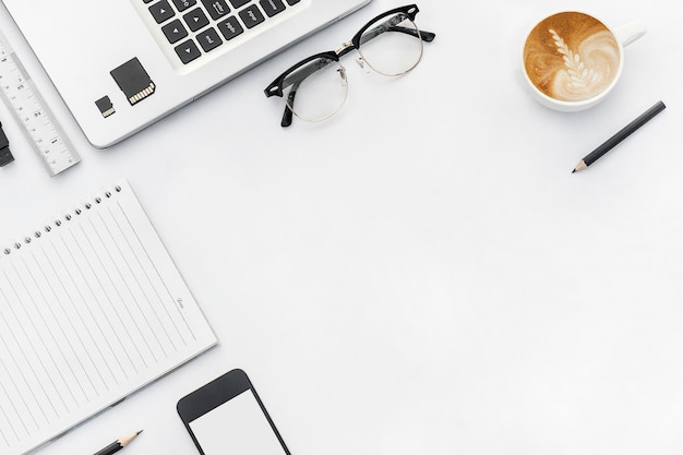 Bezpośrednio nad zdjęciem latte z technologią i materiałami biurowymi na białym stole