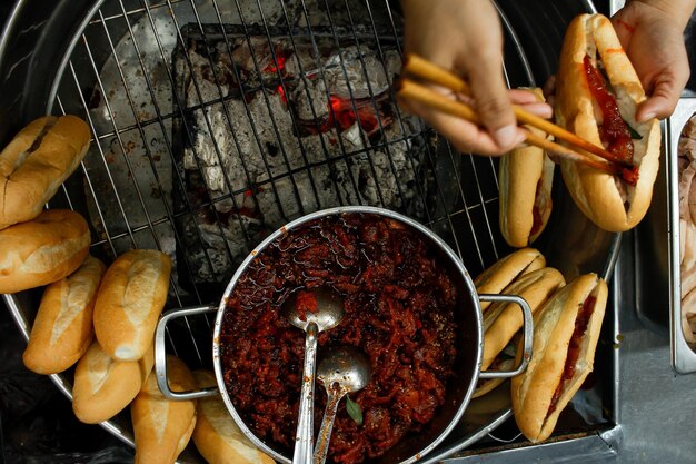 Bezpośrednio powyżej widok rąk wypełniających duszoną wieprzowinę w banhmi na nocnym targu w mieście Hue w Wietnamie