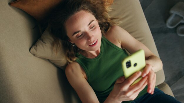 Zdjęcie beztroska dziewczyna rozmawia przez telefon mieszkanie zbliżenie uśmiechnięta kobieta leżąca na kanapie