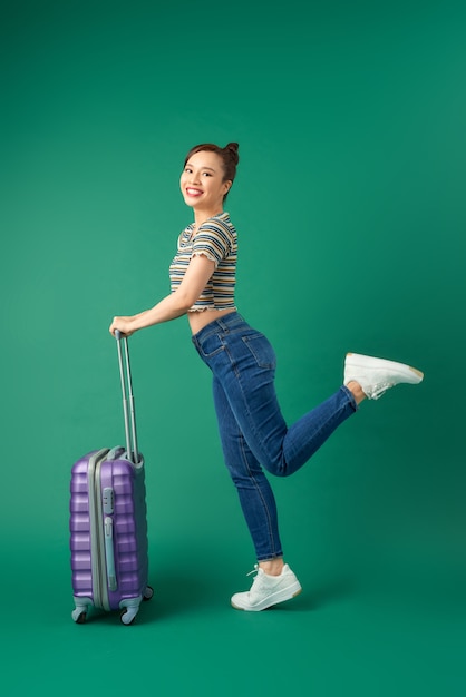 Beztroski młoda kobieta azjatyckich stwarzających z walizką na białym tle nad zielonym.
