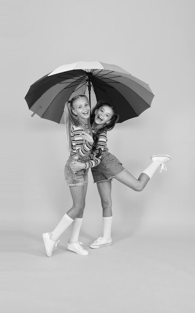 Beztroskie i szczęśliwe dwoje szczęśliwych dzieci żółte tło dzieci cieszą się deszczową jesienią jesień moda dziecięca czują się bezpiecznie i komfortowo Dobry nastrój przy każdej pogodzie mała dziewczynka pod kolorowym parasolem
