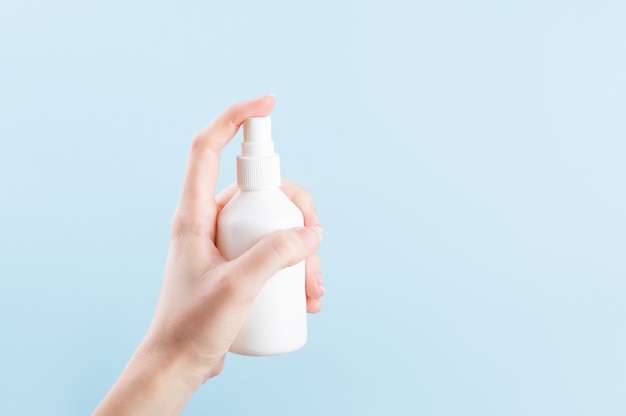 Biała butelka na produkty antyseptyczne z dozownikiem. Kobieca ręka naciskająca na niemarkowy plastikowy pojemnik