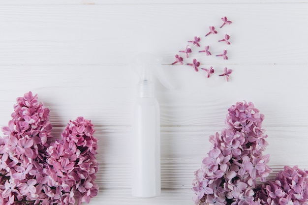Biała butelka perfum z sprayem kwiatów bzu na różowym tle