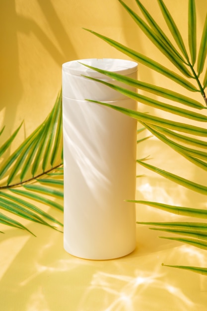 Biała butelka szamponu na żółtym tle z liśćmi palmowymi i akcentami wodnymi
