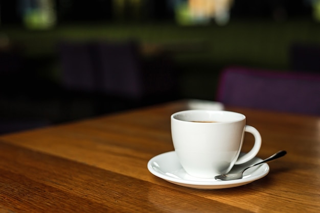 Biała filiżanka czarnej kawy, biały spodek, łyżka, drewniany stół, w kawiarni