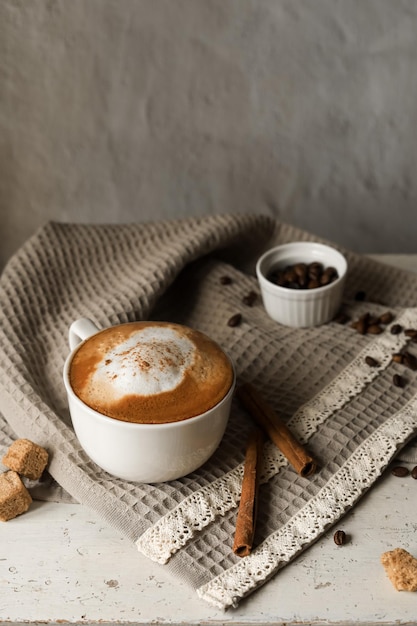 Biała filiżanka gorącego napoju kawowego z pianką i ziarnami kawy w przytulnej domowej atmosferze