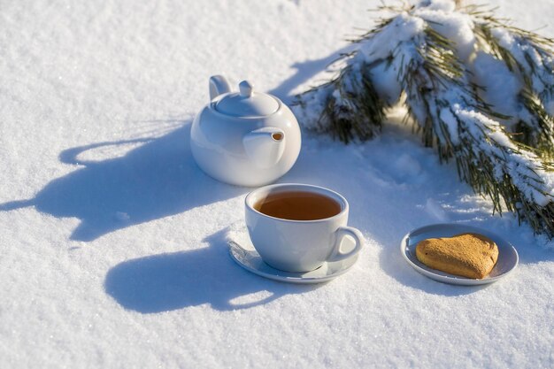 Biała filiżanka gorącej herbaty i czajniczek na łóżku ze śniegu i białego tła z bliska