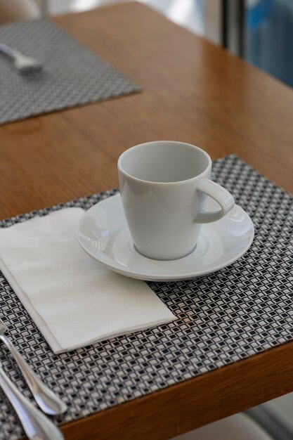 Zdjęcie biała filiżanka i spodek do kawy na serwetce na kuchennym drewnianym stole miękka selektywna ostrość niewyraźne tło koncepcja czas na herbatę hobby zbliżenie białego ceramicznego kubka z łyżką na białej serwetce