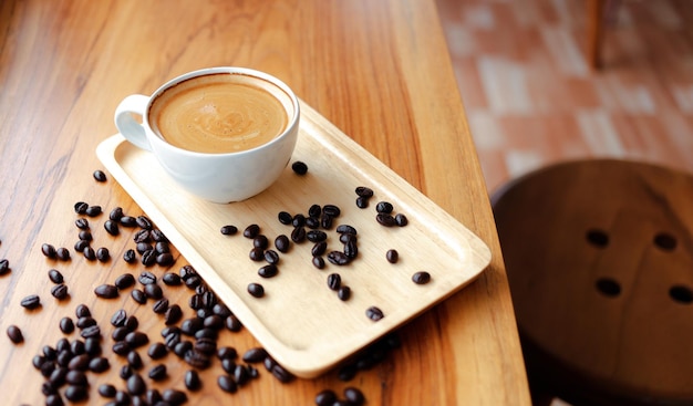 Biała filiżanka kawy espresso i palonych ziaren kawy na drewnianym blacie w kawiarni