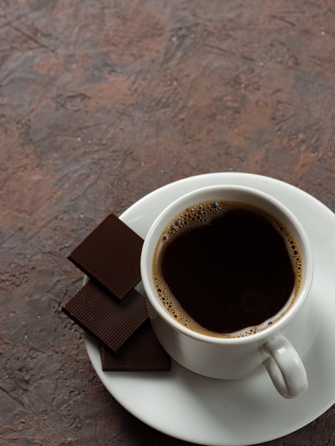 Biała filiżanka kawy i gorzka czekolada na betonowym tle