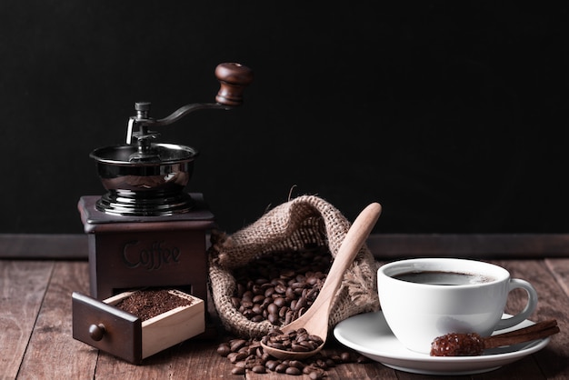 Biała filiżanka kawy, młynek do kawy i ziarna kawy w płótnie na stole z drewna
