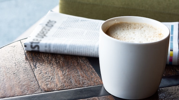 Biała filiżanka kawy z gazetą na drewnianym stole