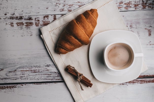 Biała Filiżanka Z Kawą, Croissant I Cynamonem Na Drewnianym Stole