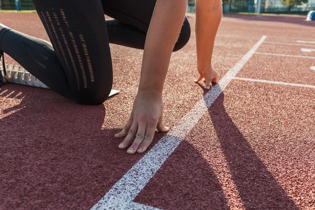 Biała kobieta w punkcie początkowym bieżni lekkoatletycznej ręce na linii startu i nogi na starcie