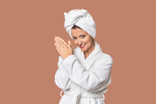 Biała kobieta w szlafroku i ręczniku czuje się energiczna i wygodna, pociera ręce, pewna siebie.