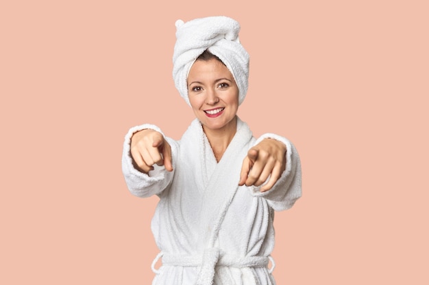 Biała kobieta w szlafroku i ręczniku z wesołym uśmiechem wskazującą do przodu