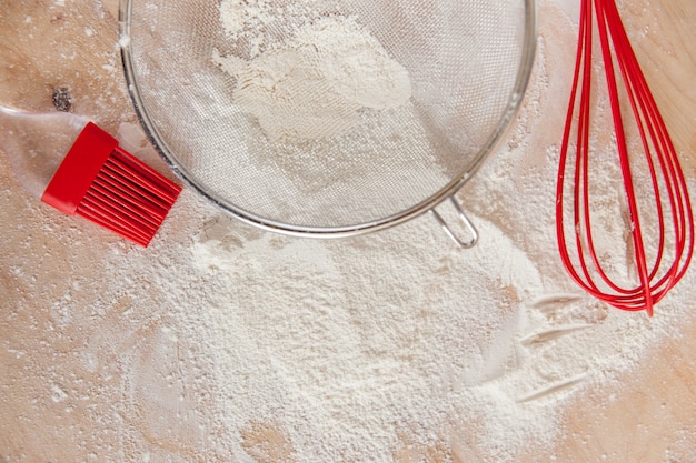 Biała mąka i czerwone silikonowe narzędzia na drewnianej desce do krojenia
