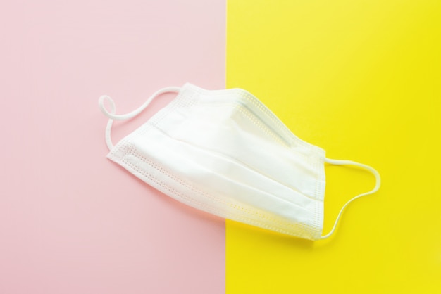 Biała maska medyczna na żółtym i różowym tle. Ochrona maseczki przed zanieczyszczeniami, wirusami, grypą, koronawirusem. Pojęcie opieki zdrowotnej. Selektywny foocus. Skopiuj miejsce