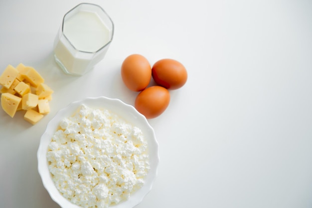 Zdjęcie biała miska z jajkami z twarogu pokrojonym w kostkę serem i szklanką mleka stoją na białym tle ...
