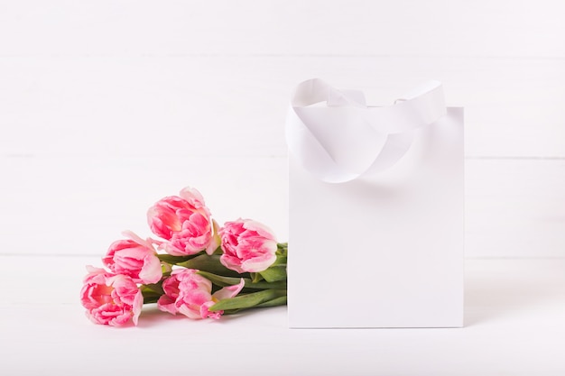 Biała papierowa torba na drewnianym tle. Bukiet pięknych różowych tulipanów. Świąteczna makieta.