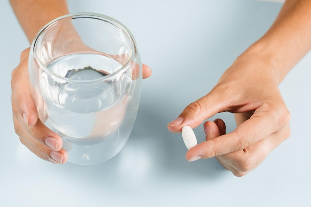 Biała pigułka dietetycznych biologicznie aktywnych suplementów i szklanka wody do codziennego spożycia tabletek na niebieskim tle