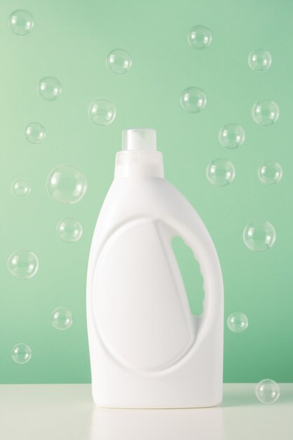 Biała plastikowa butelka płynnego detergentu do prania lub wybielacza lub zmiękczacza do tkanin z latającymi bąbelkami. Puste opakowanie makieta na środek czyszczący na zielonym tle. Dzień prania