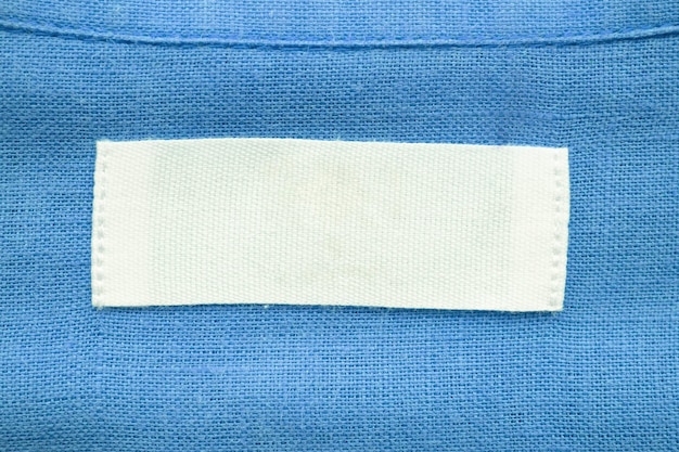 Biała pusta etykieta etykiety odzieży na niebieskim tle tekstury tkaniny lnianej koszuli