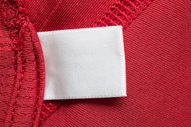 Biała pusta etykieta odzieży do prania na tle czerwonej poliestrowej koszulki sportowej